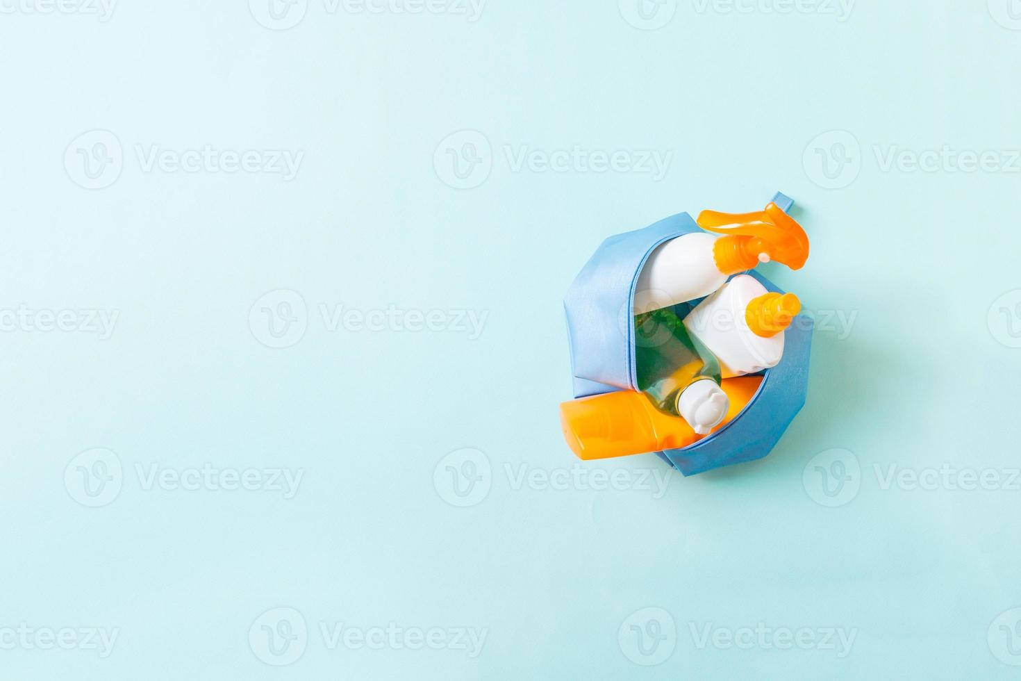 Top view of female cosmetics bag full of suncream spray, sunsreen, sunblock and body lotion and spf cream on blue background with copy space. Directly above. Bright summer concept photo