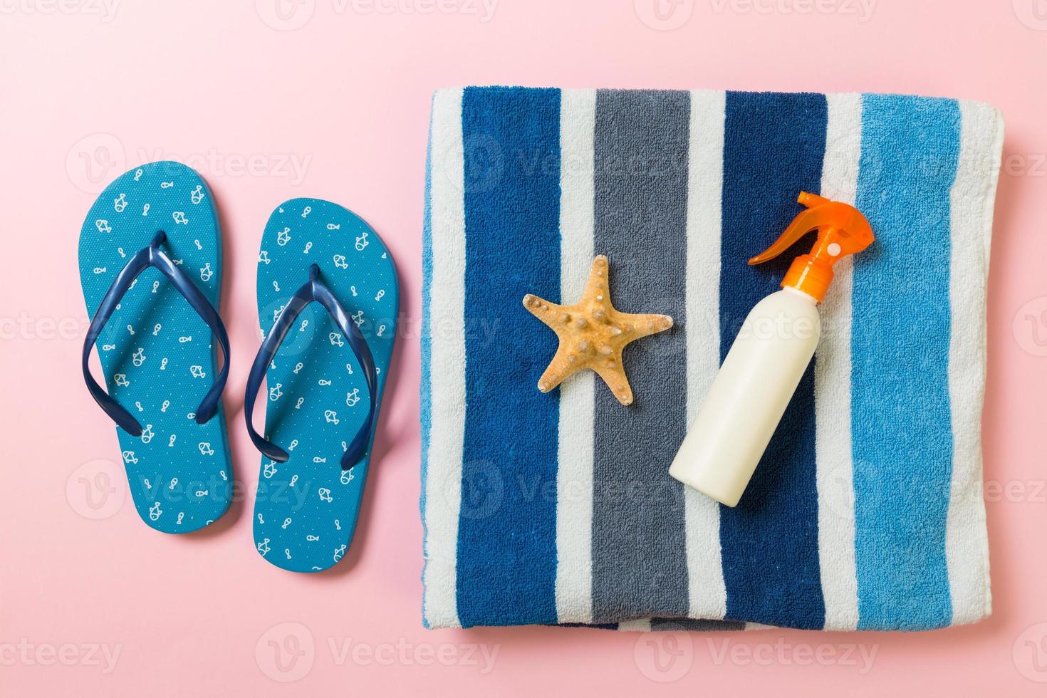 Sunscreen bottle or body spray on pink background top view flat lay with copy space. Holiday vacation travel concept with beach sea accessories photo