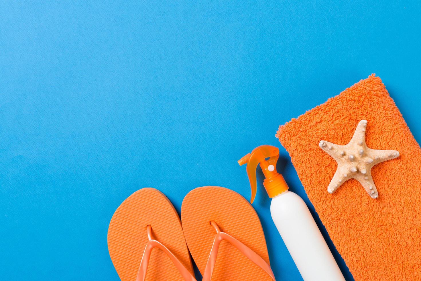 Top view of Beach flat lay accessories. sunscreen bottle with seashells, starfish, towel and flip-flop on Colored background with copy space photo