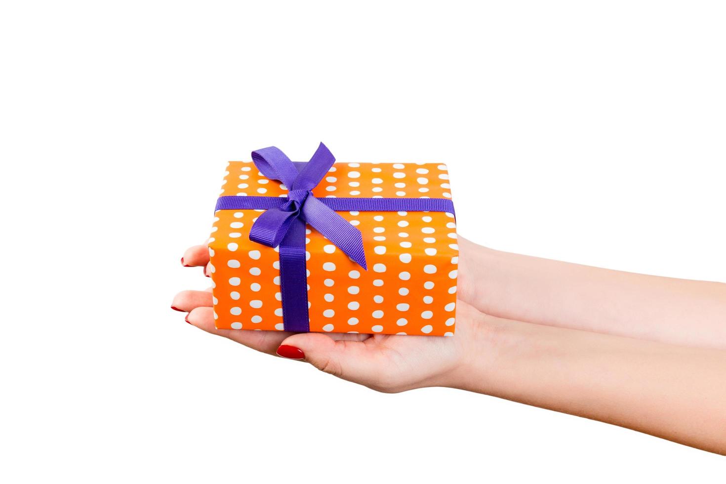 Woman hands give wrapped Christmas or other holiday handmade present in orange paper with purple ribbon. Isolated on white background, top view. thanksgiving Gift box concept photo