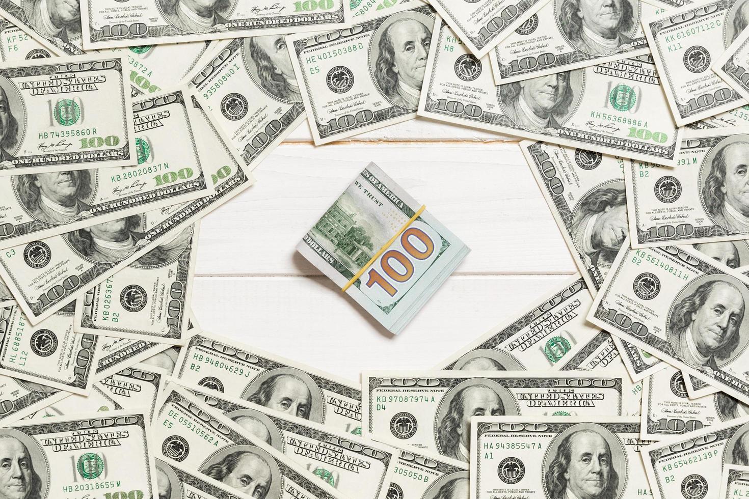 Frame of one hundred dollar bills with stack of money in the middle. Top view of business concept on white wooden background with copy space photo