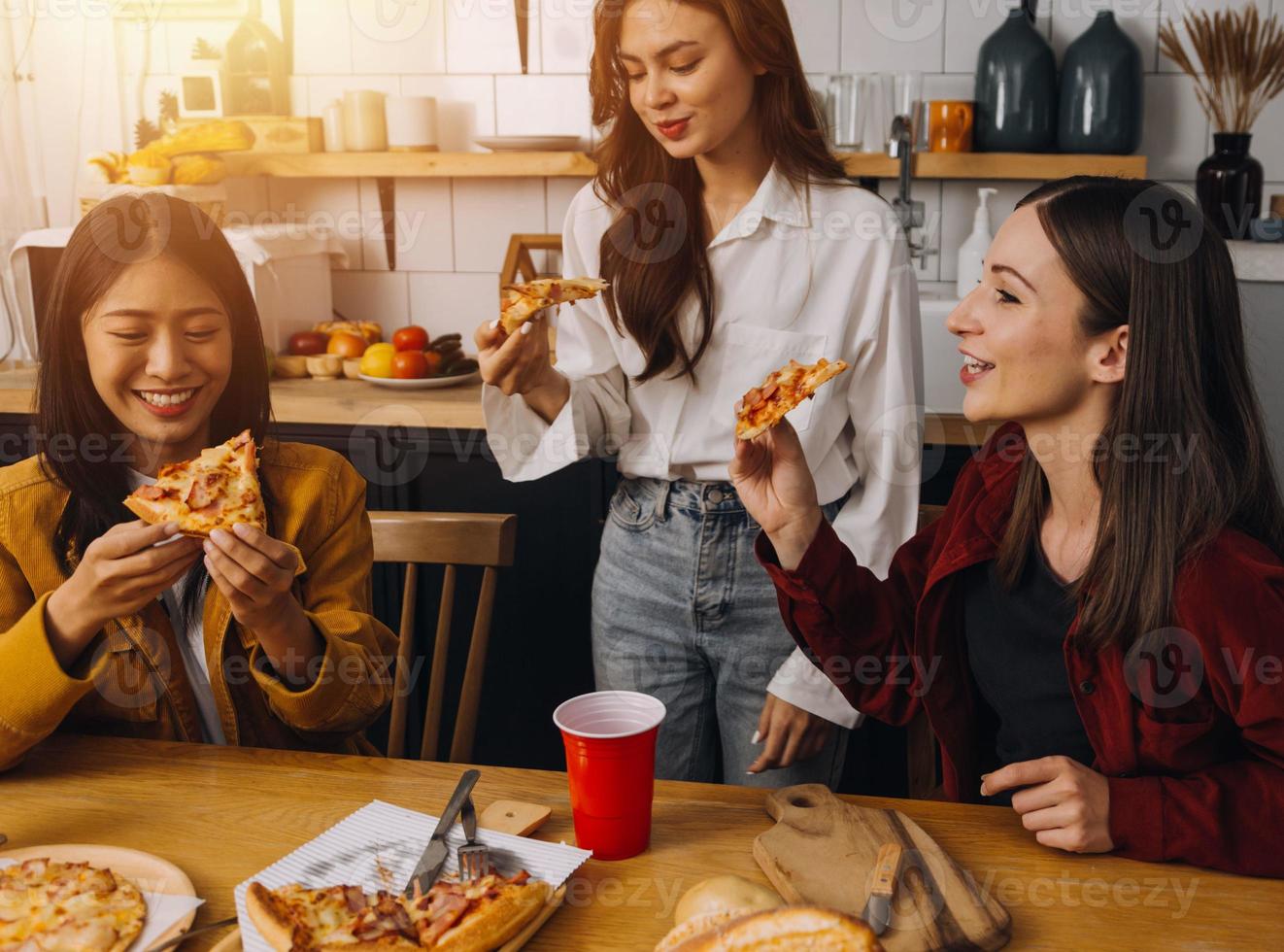 Young woman eating pizza and laughing while sitting with her friends in a restaurant. Group of friends enjoying while having food and drinks at cafe. photo