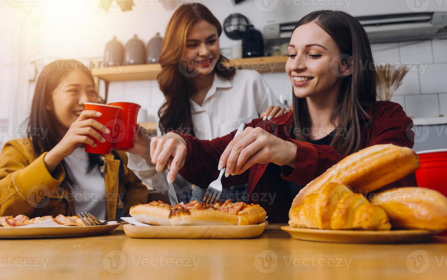 Young woman eating pizza and laughing while sitting with her friends in a restaurant. Group of friends enjoying while having food and drinks at cafe. photo