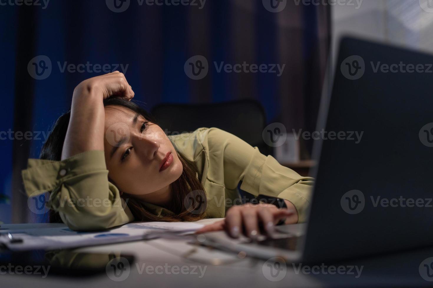 Sleepy exhausted asian young businesswoman working at office desk with her laptop, her eyes are closing. Overtime working concept photo