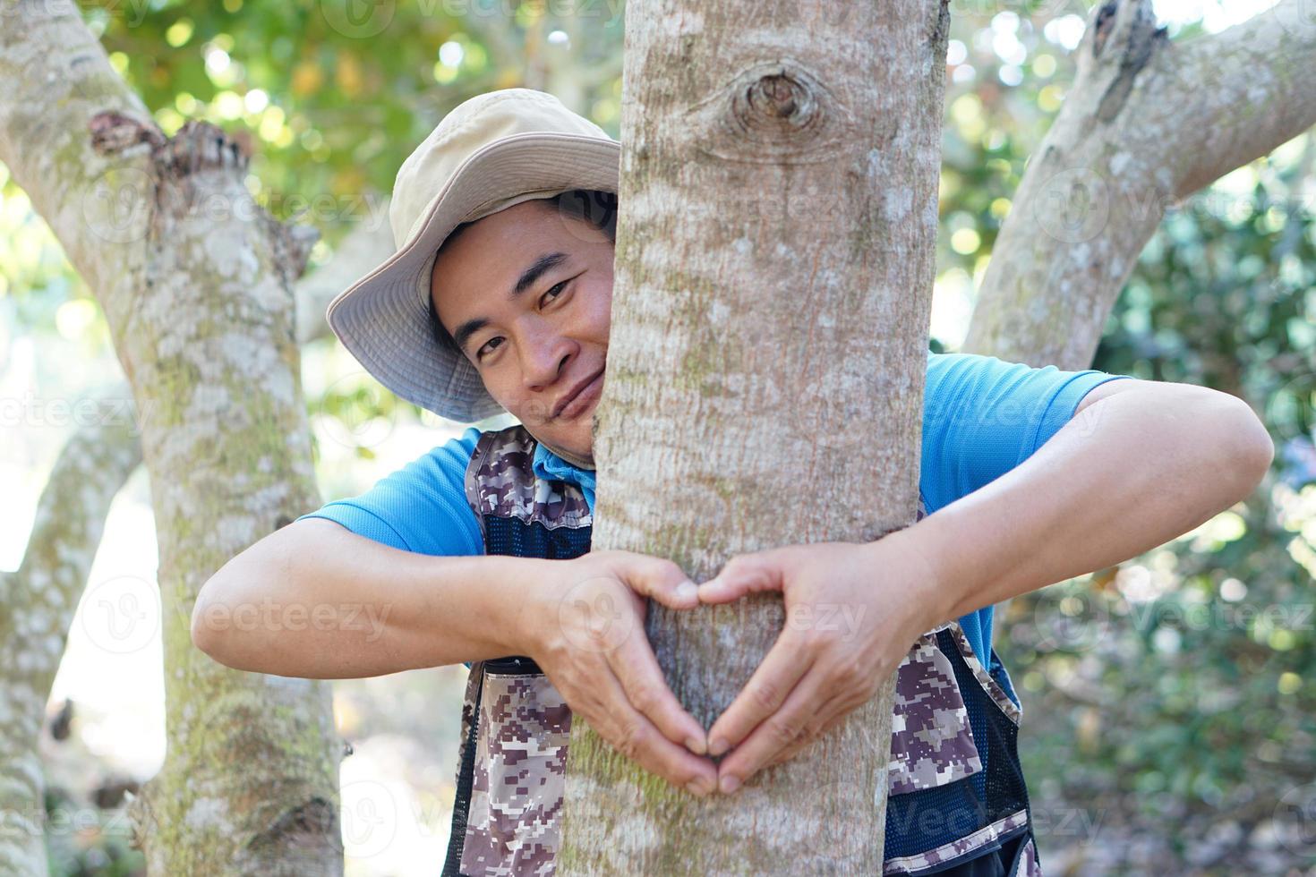 Handsome Asian man botanist hugs trunk of tree in forest, make sign of heart shape. Concept, Love nature and protecting, Forest ,ecology and environment conservation. . photo