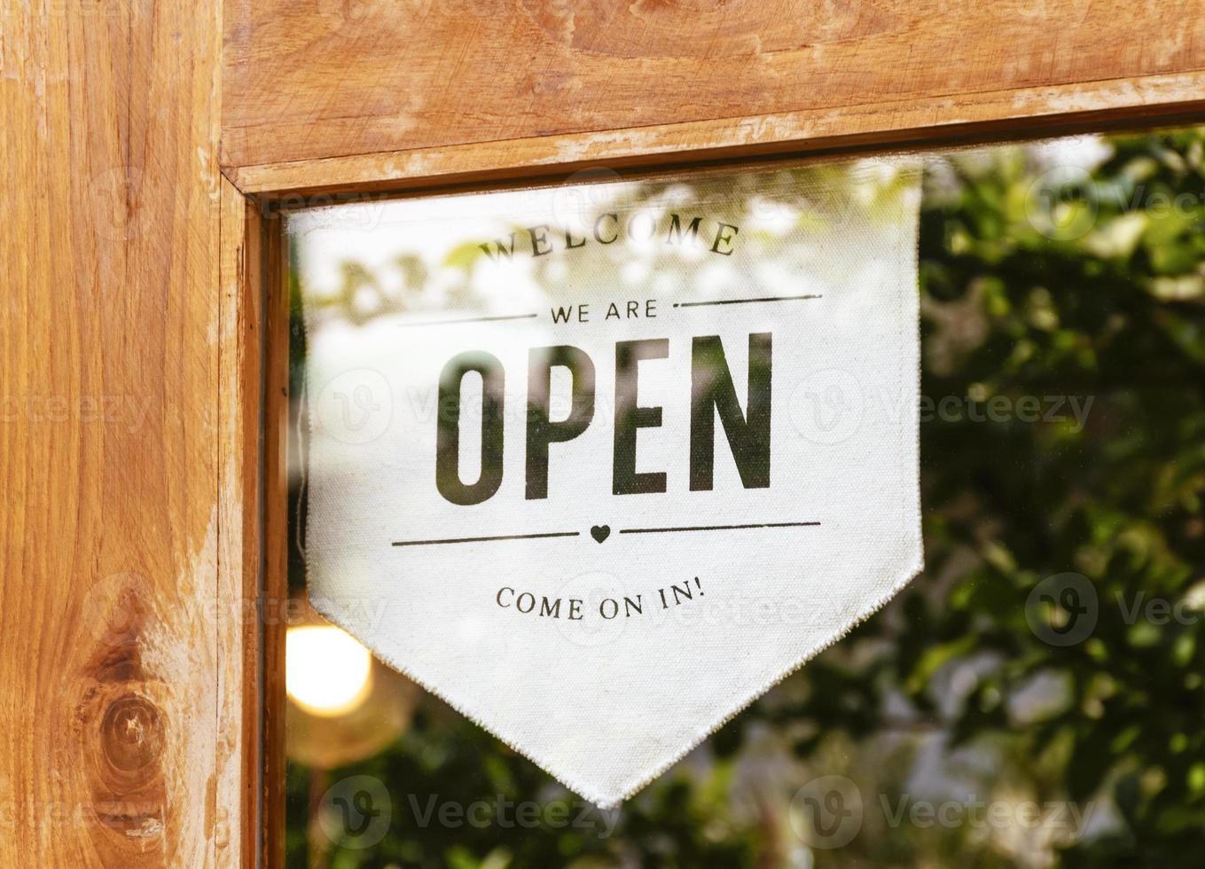 cartel colgante con mensaje de bienvenida abierto en la puerta de cristal en la cafetería foto