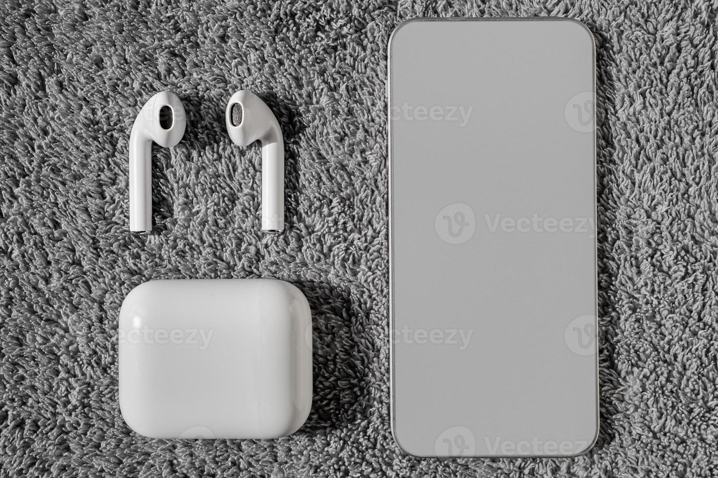 Top view of a thin smartphone with a gray screen for a banner next to wireless white headphones on a gray velvet background. Distance learning, work from home or online courses or support system. photo