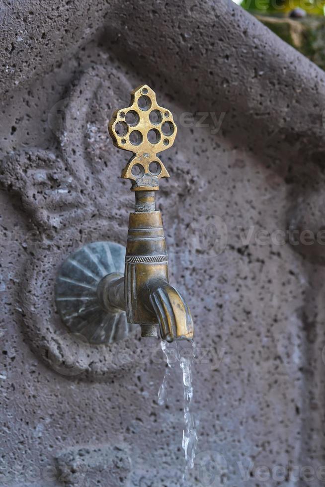 Water flows from an old copper faucet, a vertical shot of a sink in a public place on the street of the old city in Turkey, travel time, an idea for a background photo