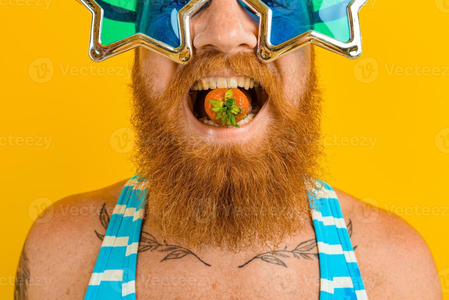 man with beard and sunglasses eats a strawberry photo