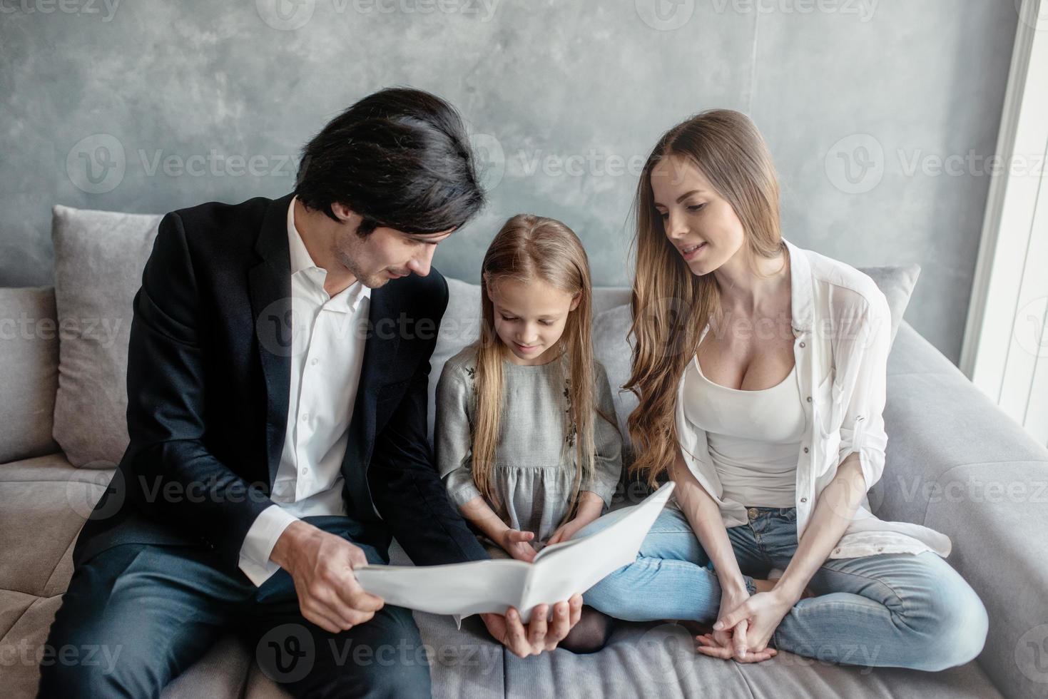 contento pequeño niña lee un libro con su padres foto