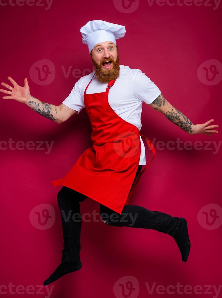 contento cocinero con barba y rojo delantal saltos foto