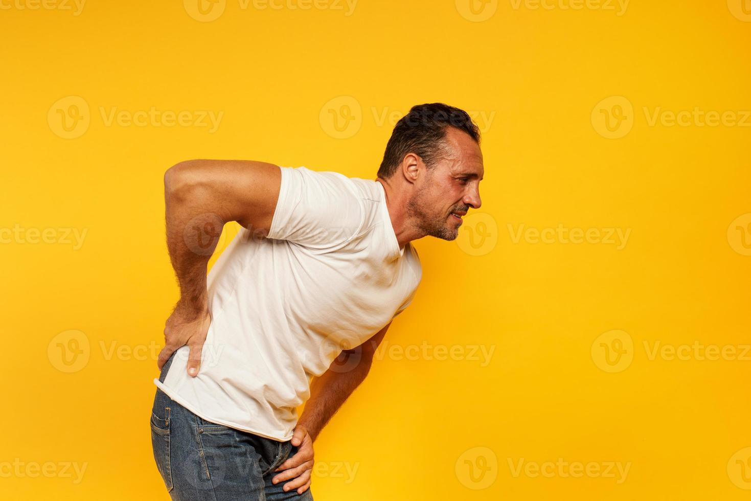 Aching man with back pain. Yellow background photo