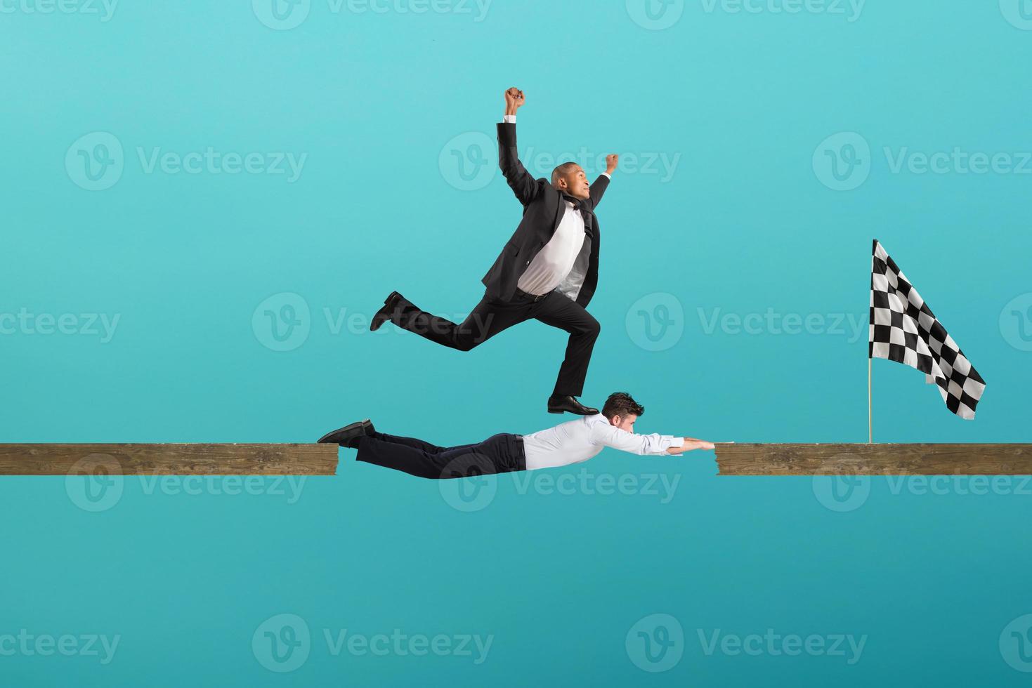 Businessman uses his body like a bridge to help his coullague to reach the flag. concept of teamwork and partnership. Cyan background photo