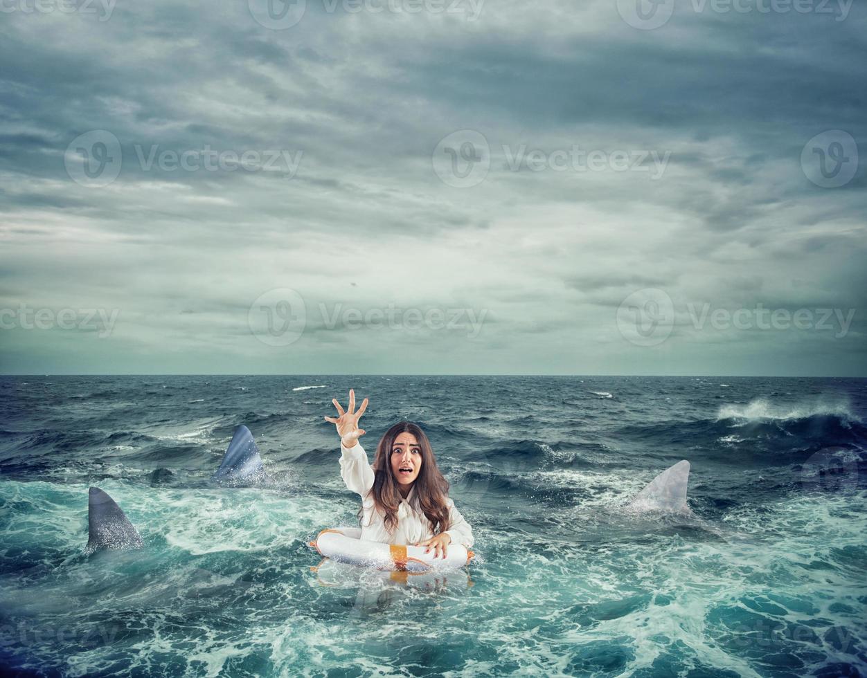Businesswoman with lifebelt surrounded by sharks asks help photo