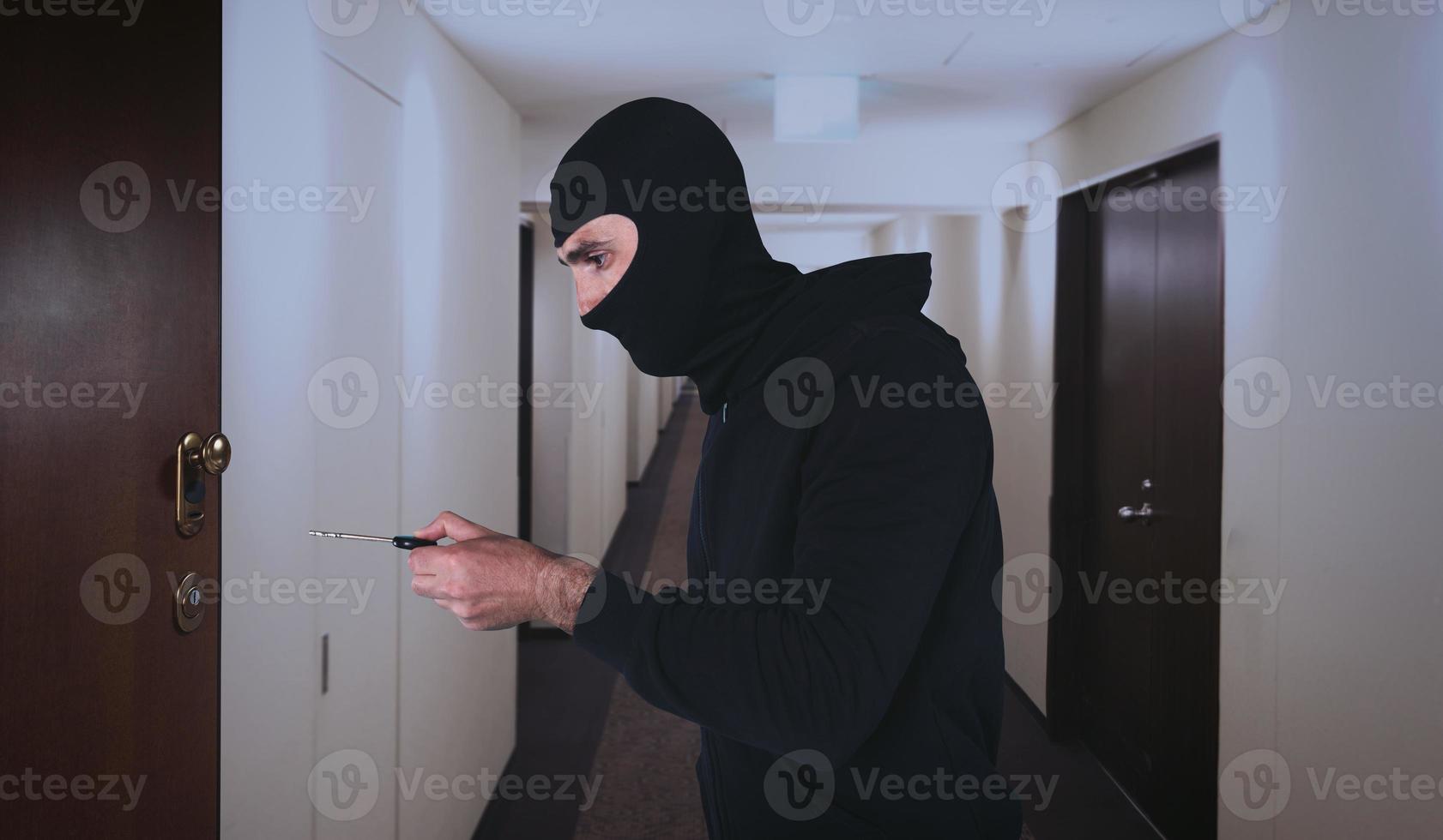 Thief with balaclava tries to open the door of apartment with a key photo