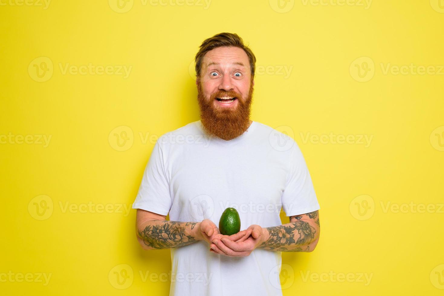 Happy man with beard and tattoos holds an avocado photo