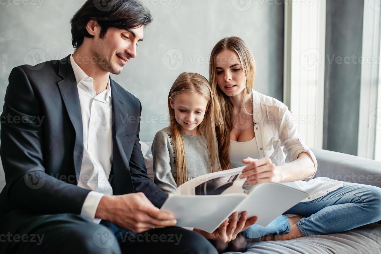 contento pequeño niña lee un libro con su padres foto