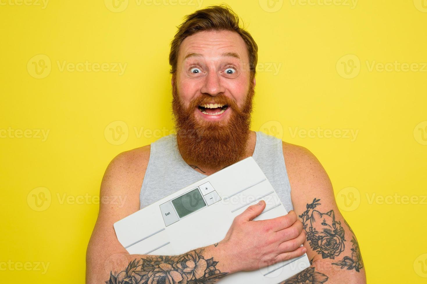 Happy man with beard and tattoos holds an electronic balance photo