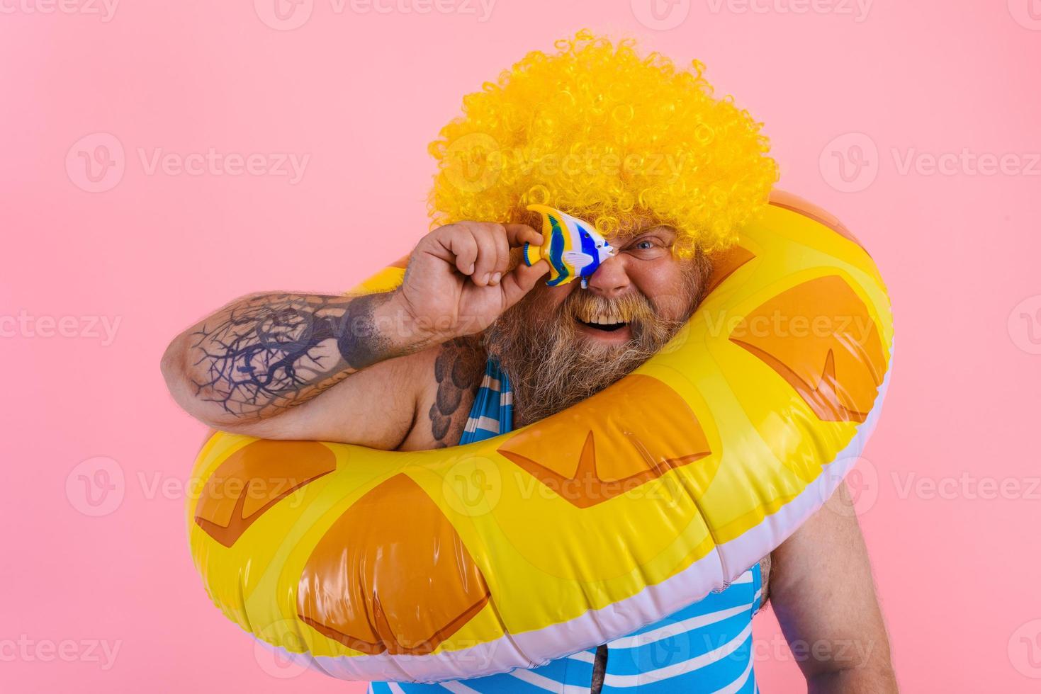 Fat man with wig in head is ready to swim with a donut lifesaver photo