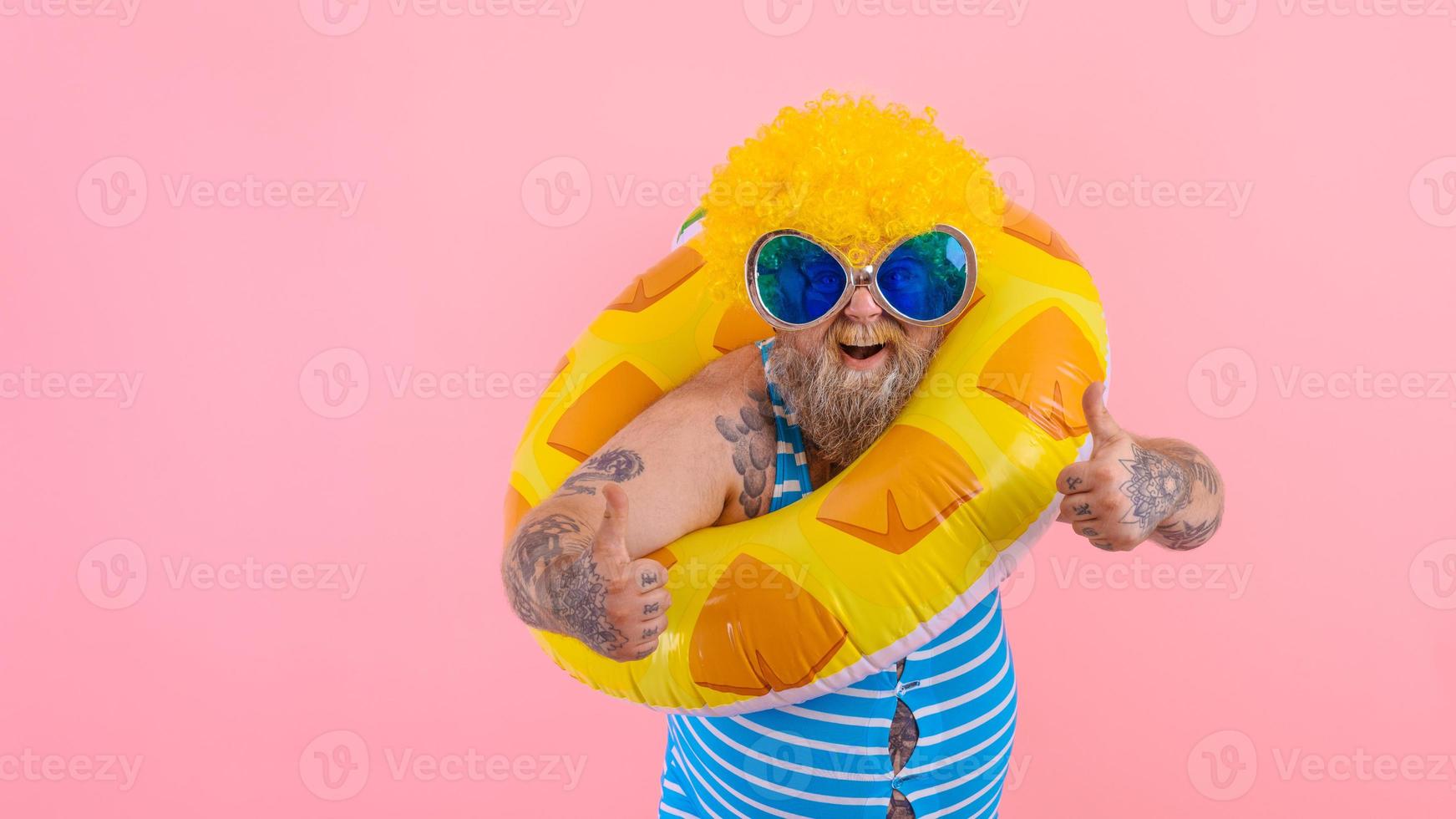 Fat happy man with wig in head is ready to swim with a donut lifesaver photo