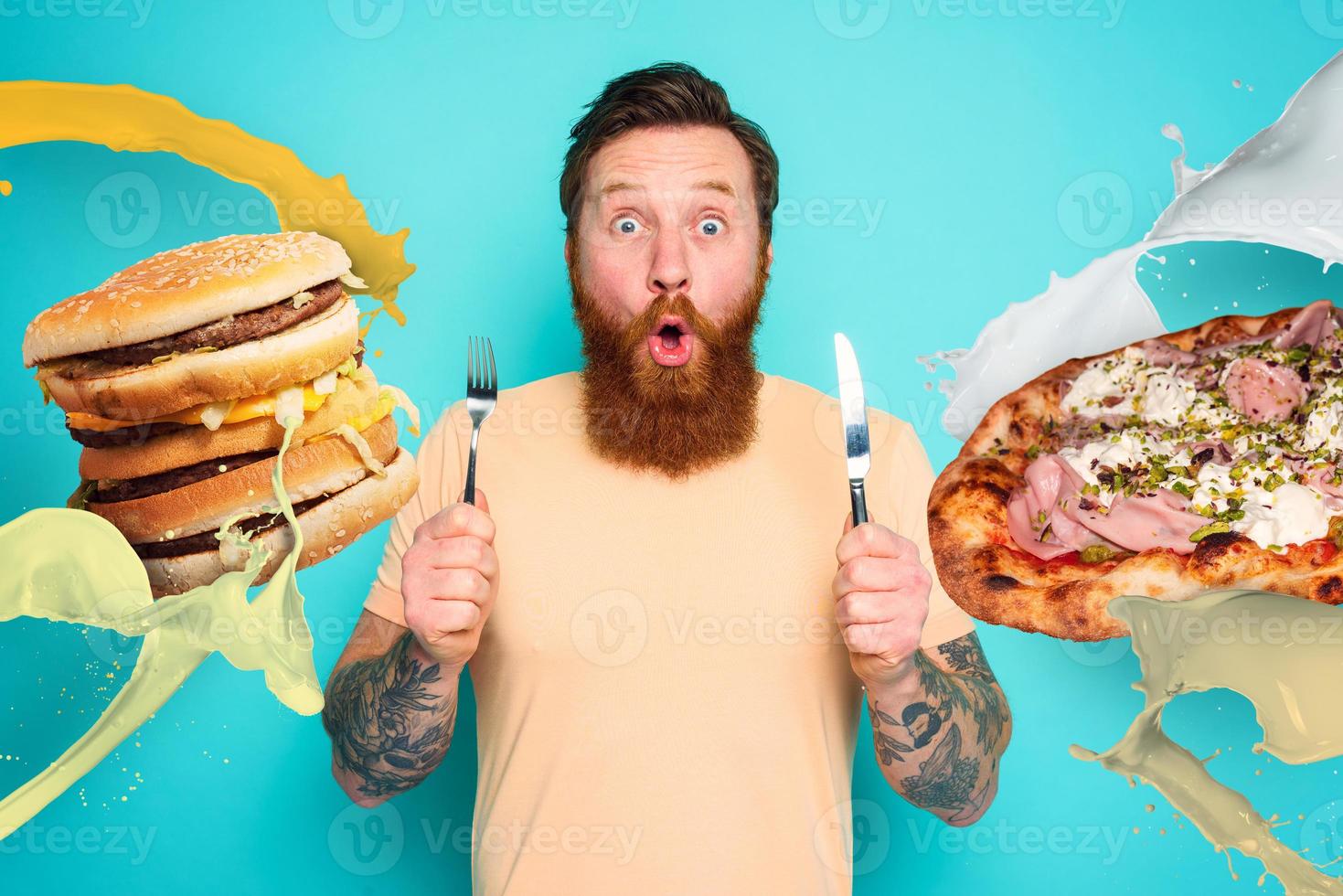 Man with tattoos is ready to eat sandwich and pizza with cutlery in hand. cyan background photo