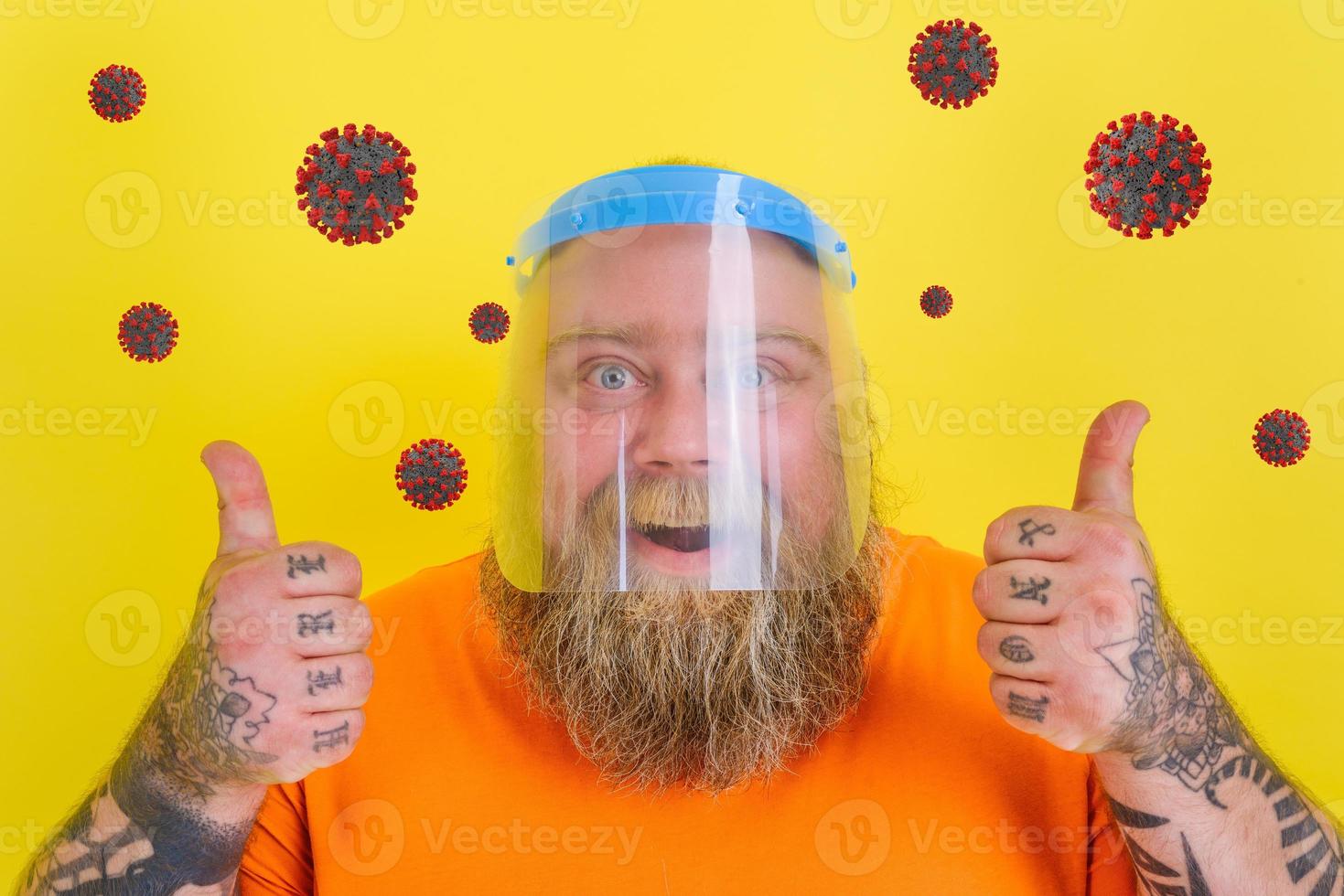 Happy man with beard and tattoos wears a protective face shield against covid-19 photo