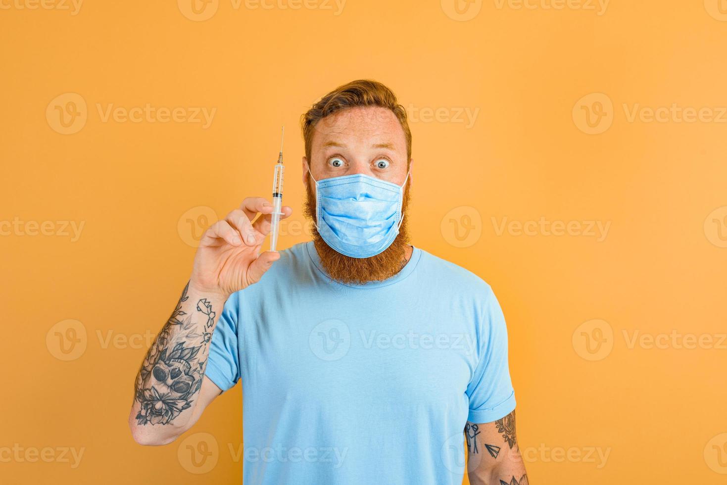 Afraid man with beard, tattoo and mask for covid-19 is ready for the virus vaccine photo
