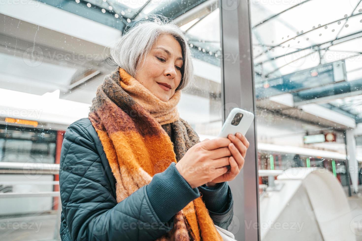 Senior woman send message with a mobile phone and waits for a train photo