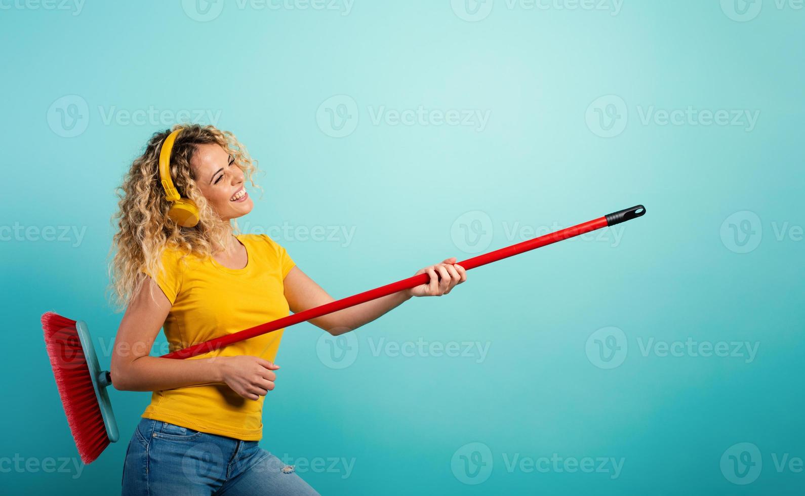 Girl with headset use the broom like a guitar. Cyan background photo