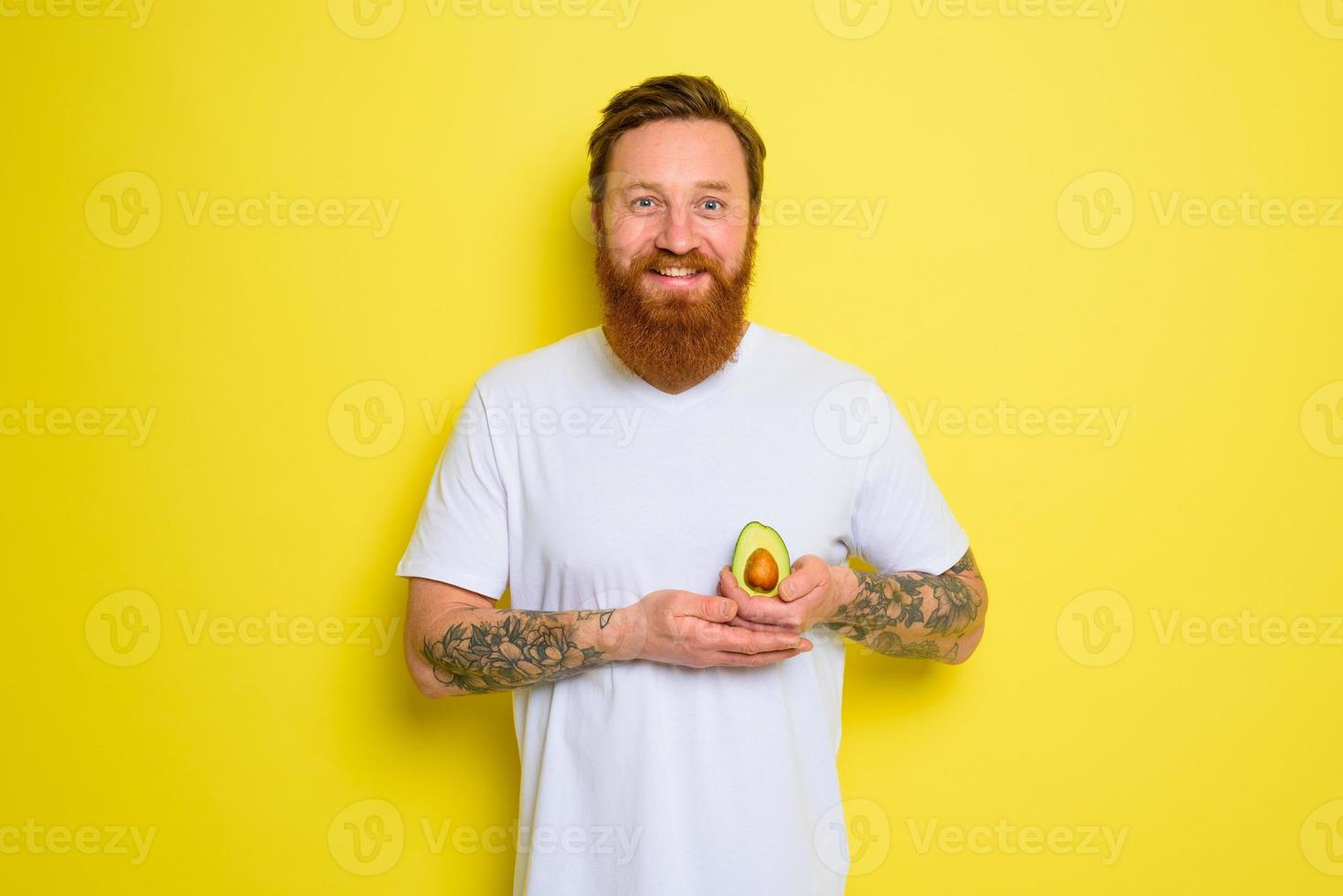 Happy man with beard and tattoos holds an avocado photo