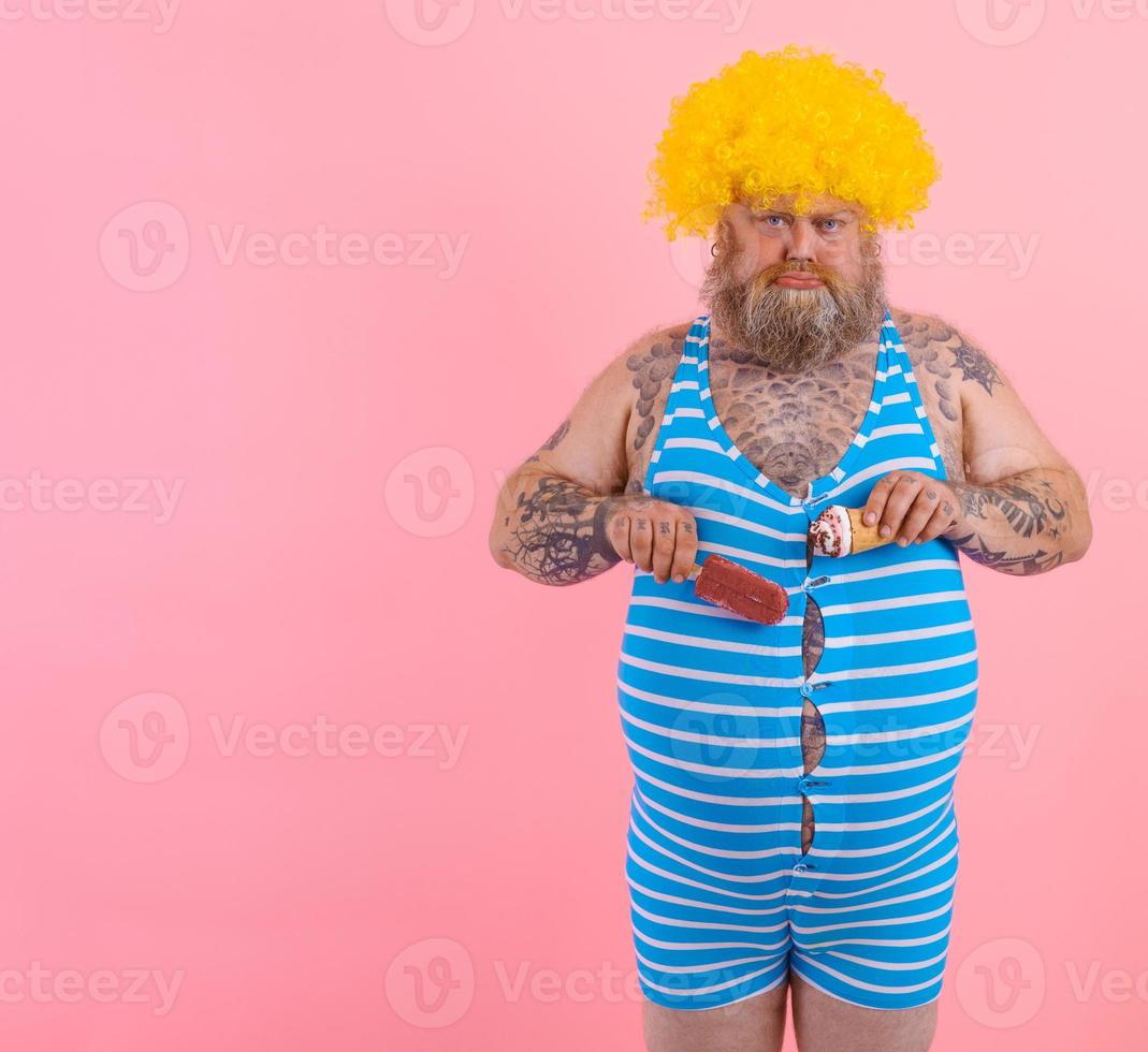 Fat man with beard and wig eats a popsicle and an icecream photo
