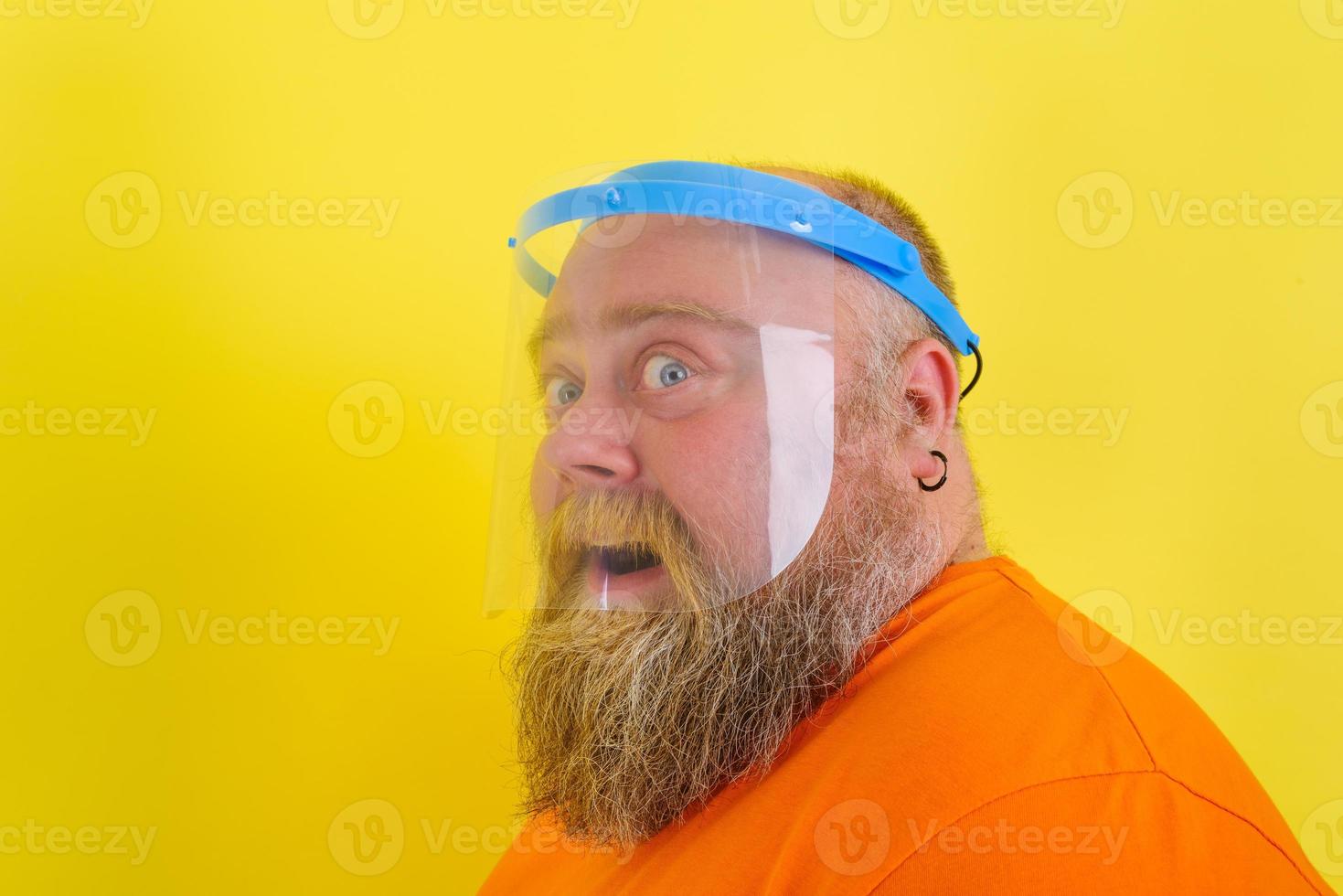 Amazed man with beard and tattoos wears a protective face shield against covid-19 photo