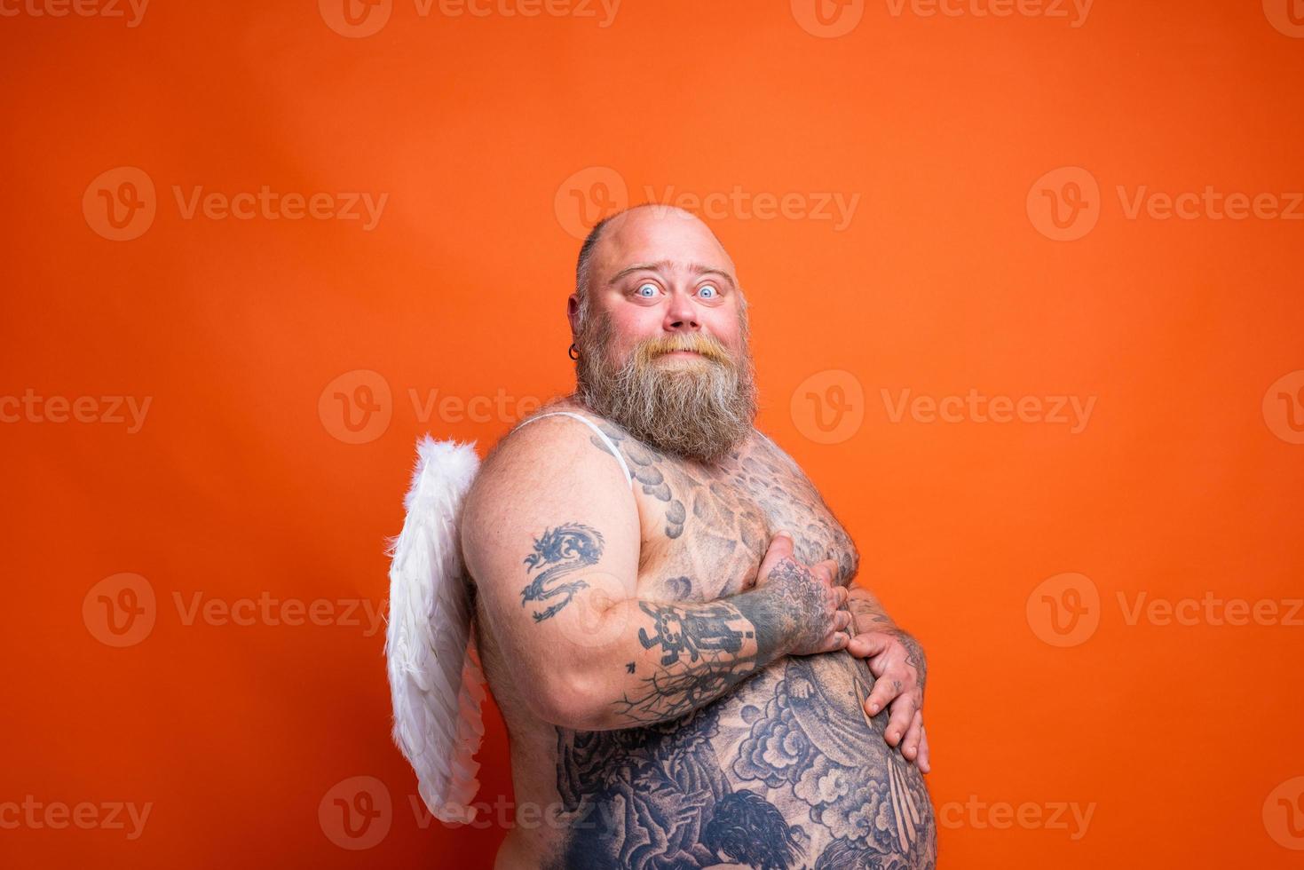 Fat afraid man with beard ,tattoos and wings acts like an angel photo