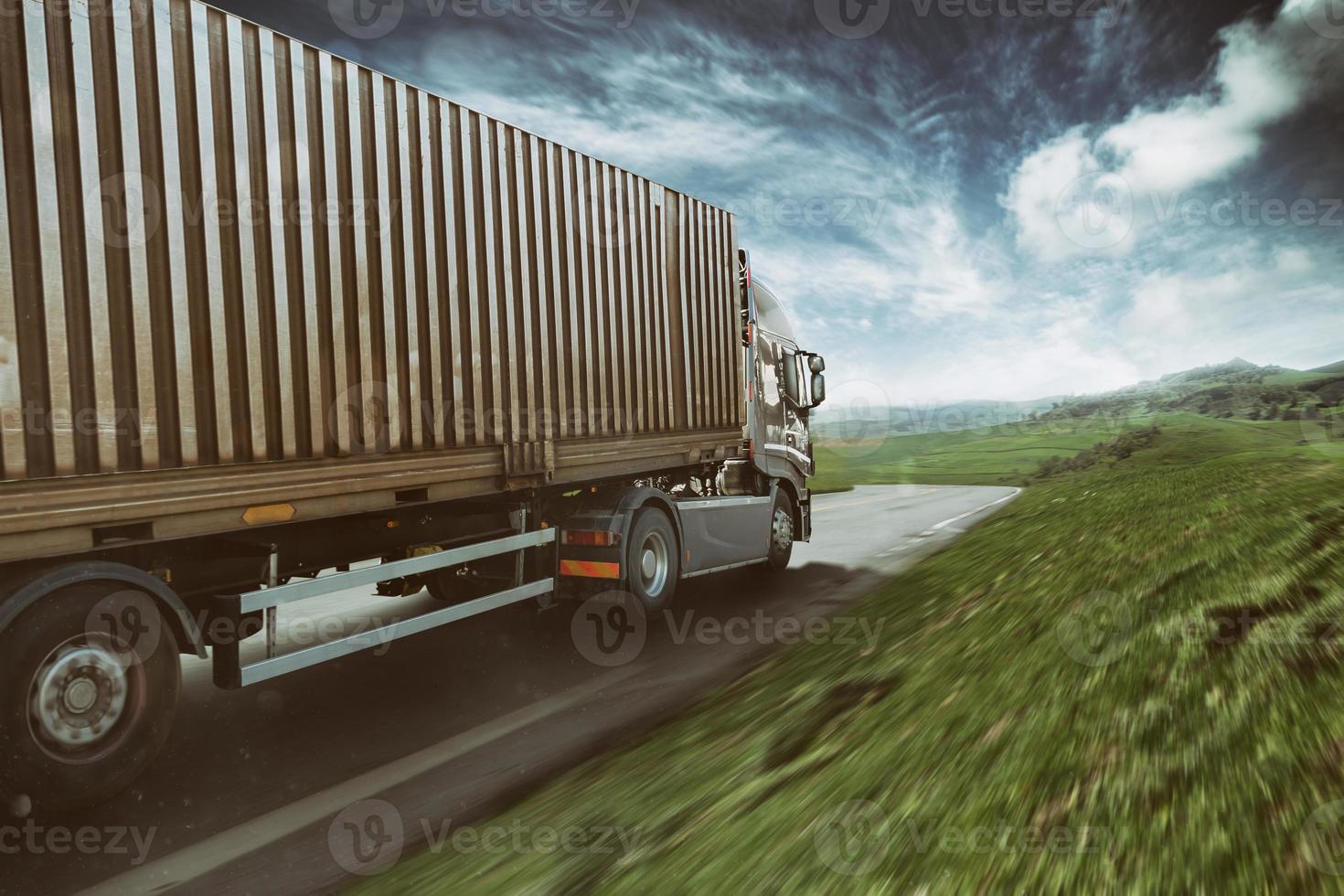 Grey truck moving fast on the road in a natural landscape with cloudy sky photo