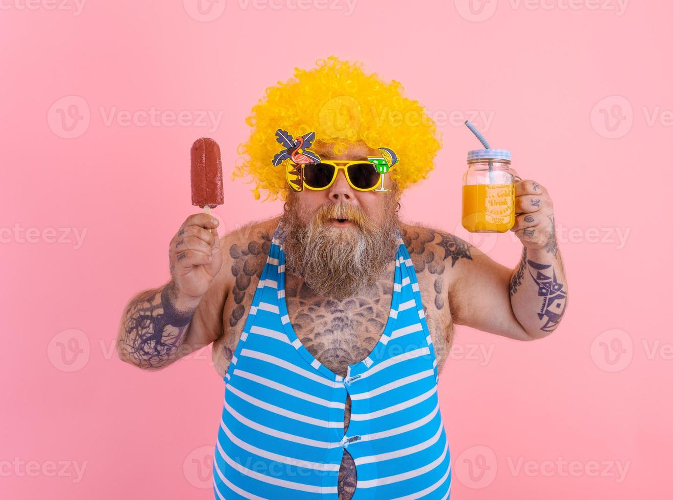 Fat surprised man with beard and wig eats a popsicle and drinks a juice fruit photo