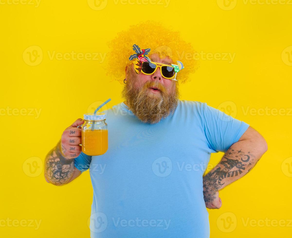 Fat happy man with wig in head and sunglasses drinks a fruit juice photo