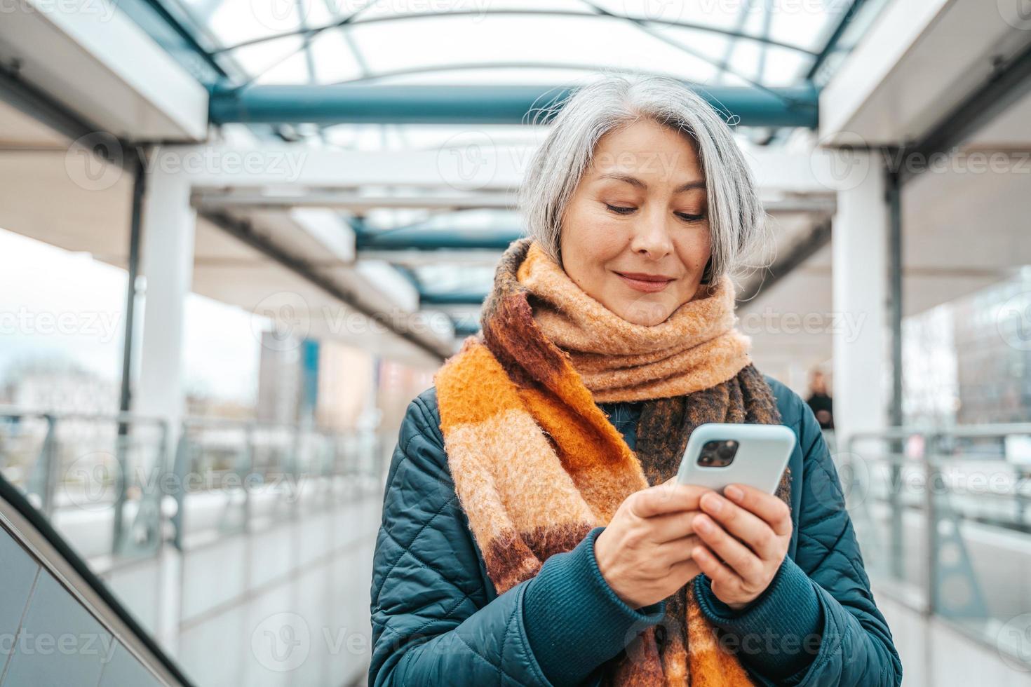 Senior woman send message with a mobile phone in a stransport station photo