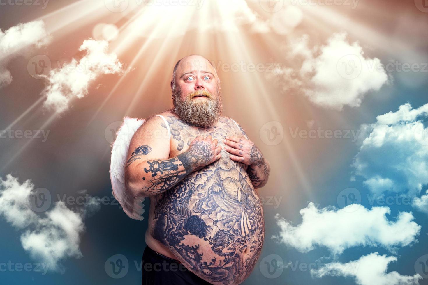 Fat amazed man with beard ,tattoos and wings acts like an angel photo