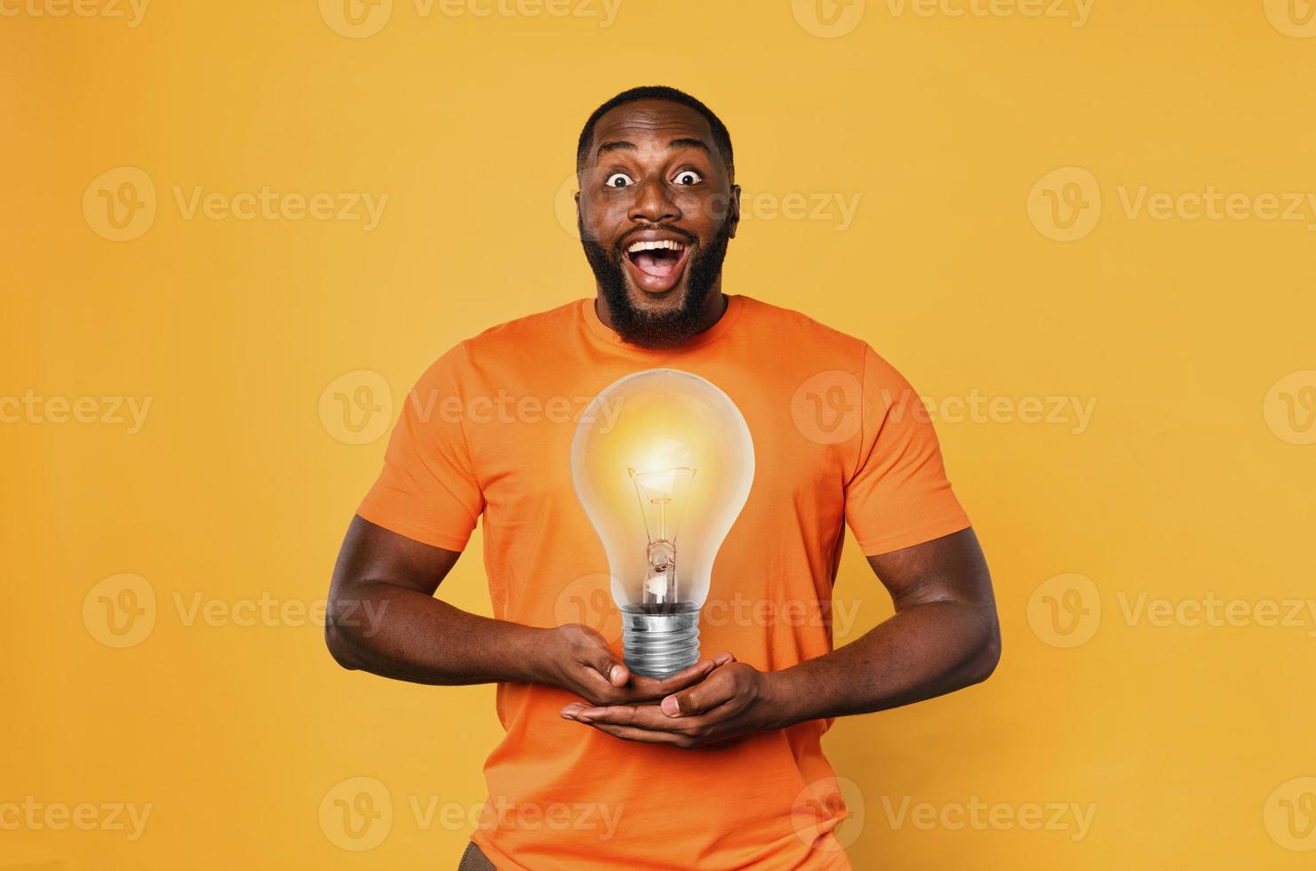 Happy afro man holds a lightbulb with hands. Concept of idea and creativity. Orange background photo