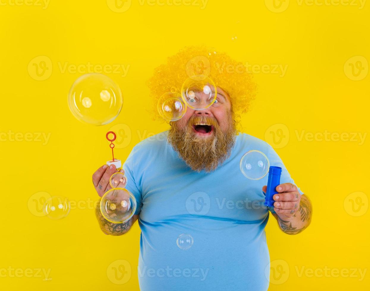 Amazed man with yellow wig in head play with bubbles soap photo