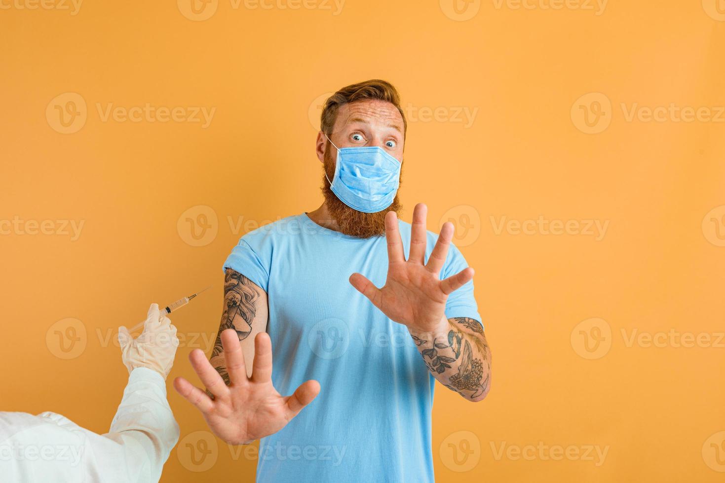Afraid man with beard, tattoo and mask for covid-19 is ready for the virus vaccine photo
