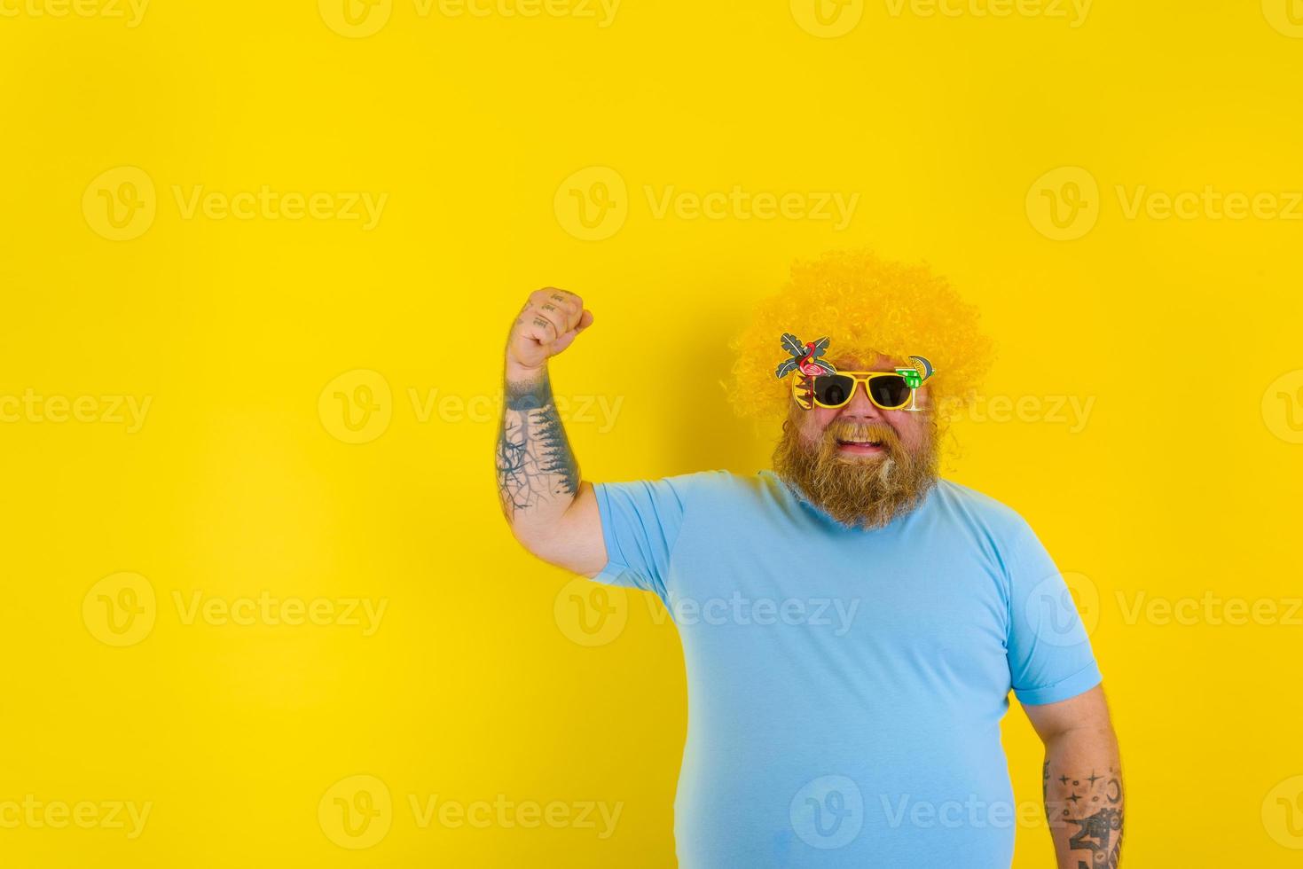 Fat man with wig in head and sunglasses shows his muscle photo