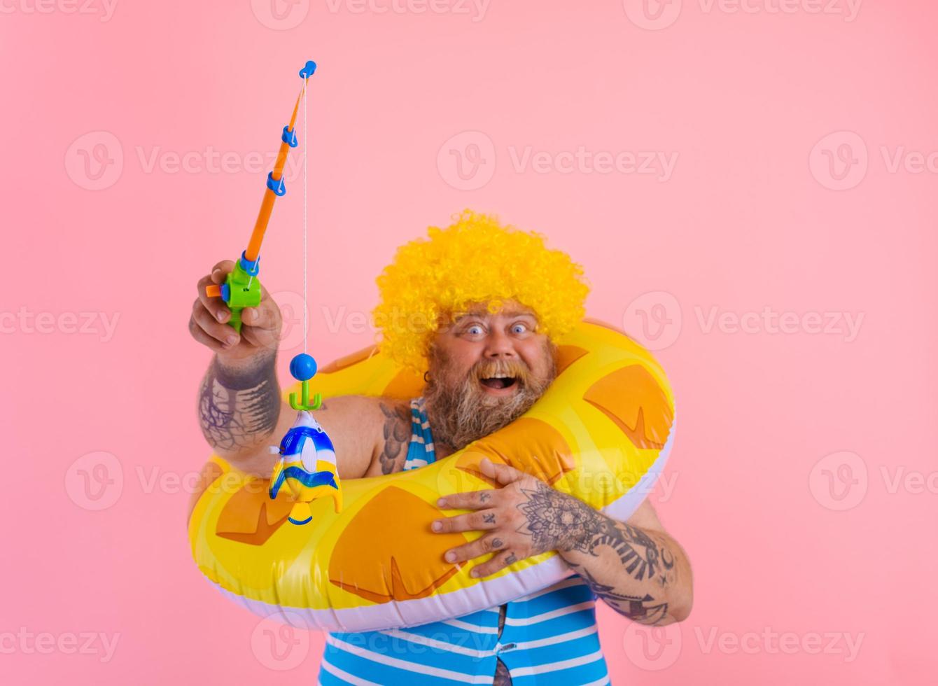 Fat happy man with wig in head plays with the fishing rod photo