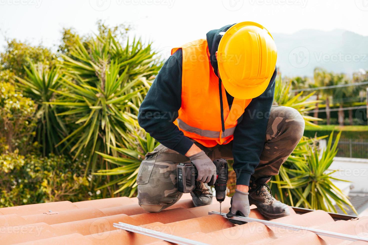 trabajador de techado con uniforme protector y guantes, herramientas para  techos, instalación de techos nuevos en construcción, taladro eléctrico  usado en techos nuevos con láminas de metal. 15632779 Foto de stock en