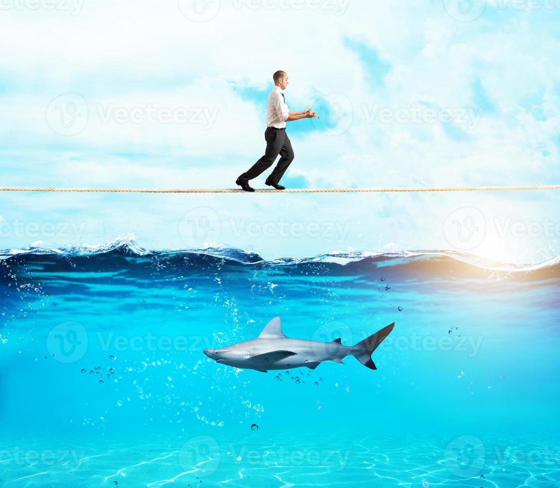 Worry man in balance walking on a rope over a shark photo