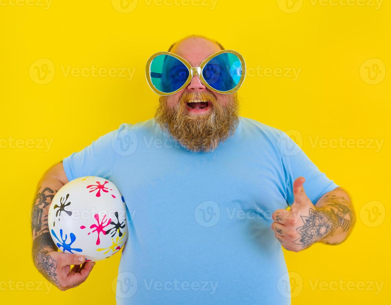 Fat man with beard and sunglasses have fun with a ball photo