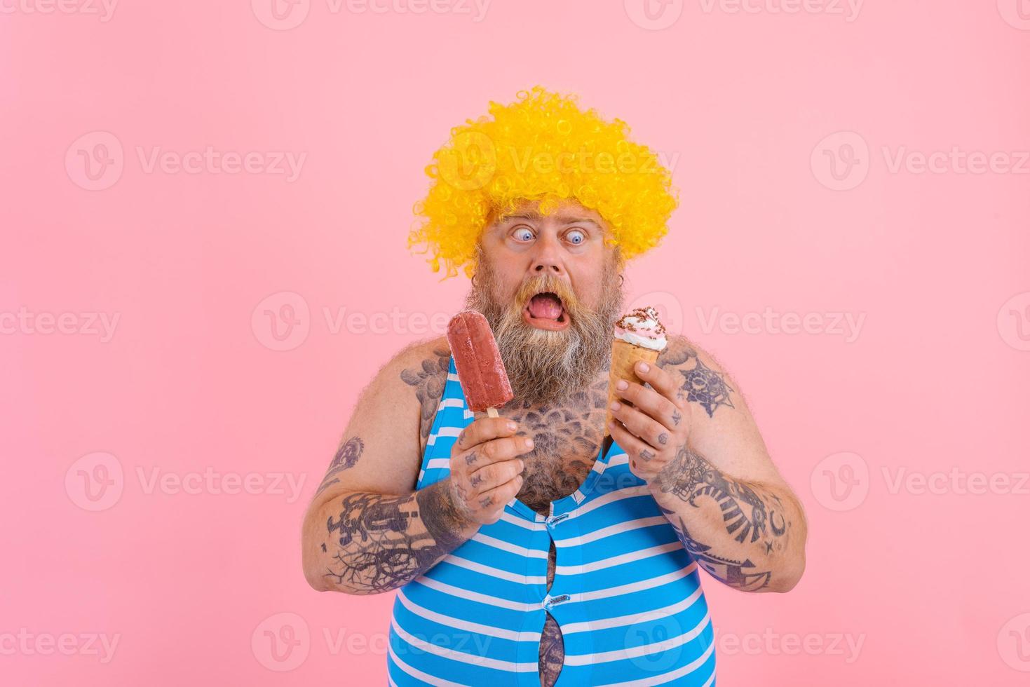 Fat man with beard and wig eats a popsicle and an icecream photo