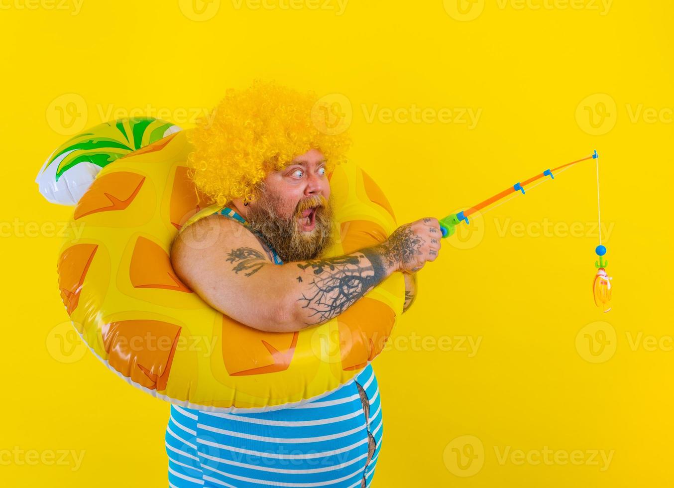 Fat amazed man with wig in head plays with the fishing rod photo