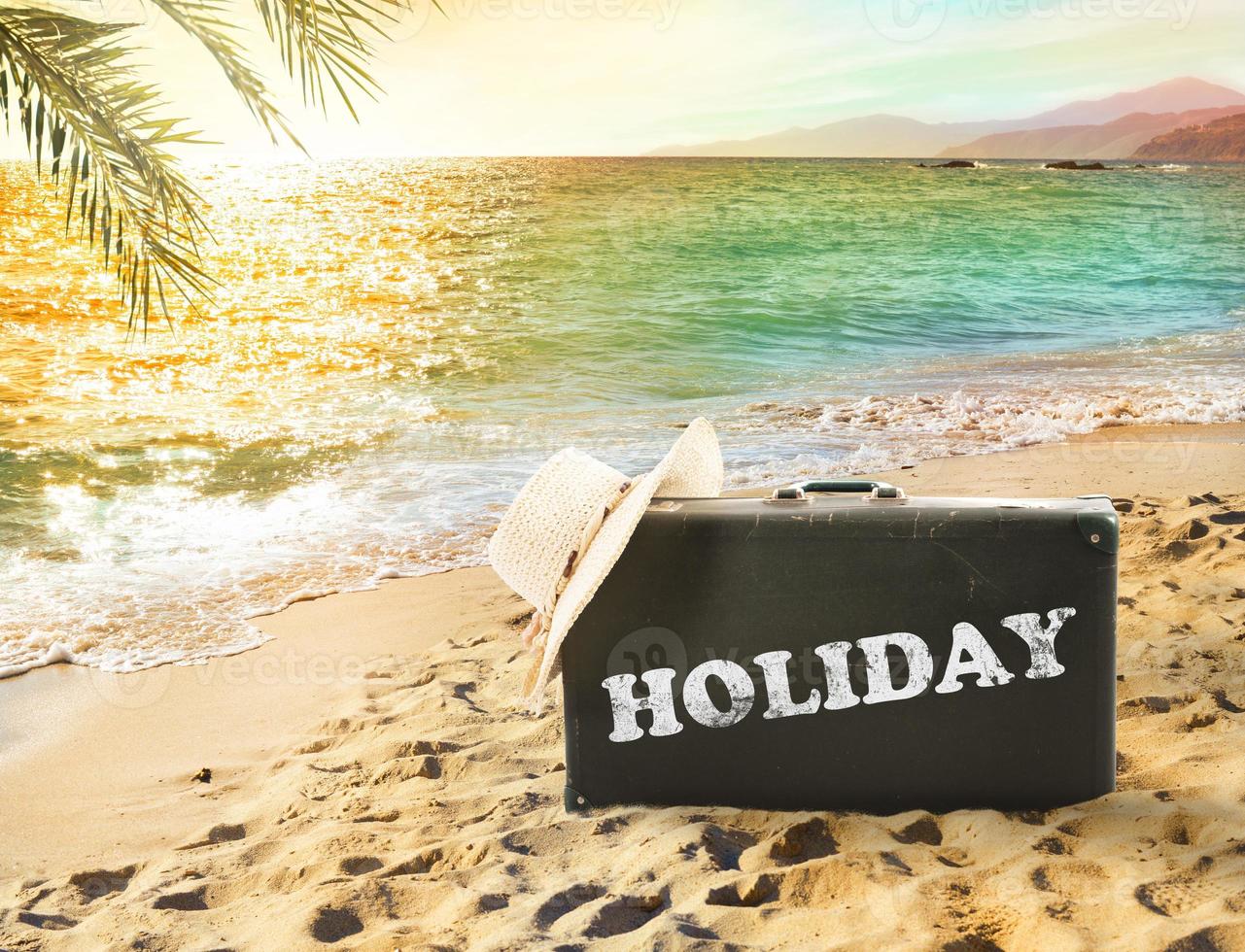 Suitcase in a tropical beach with holiday writing photo