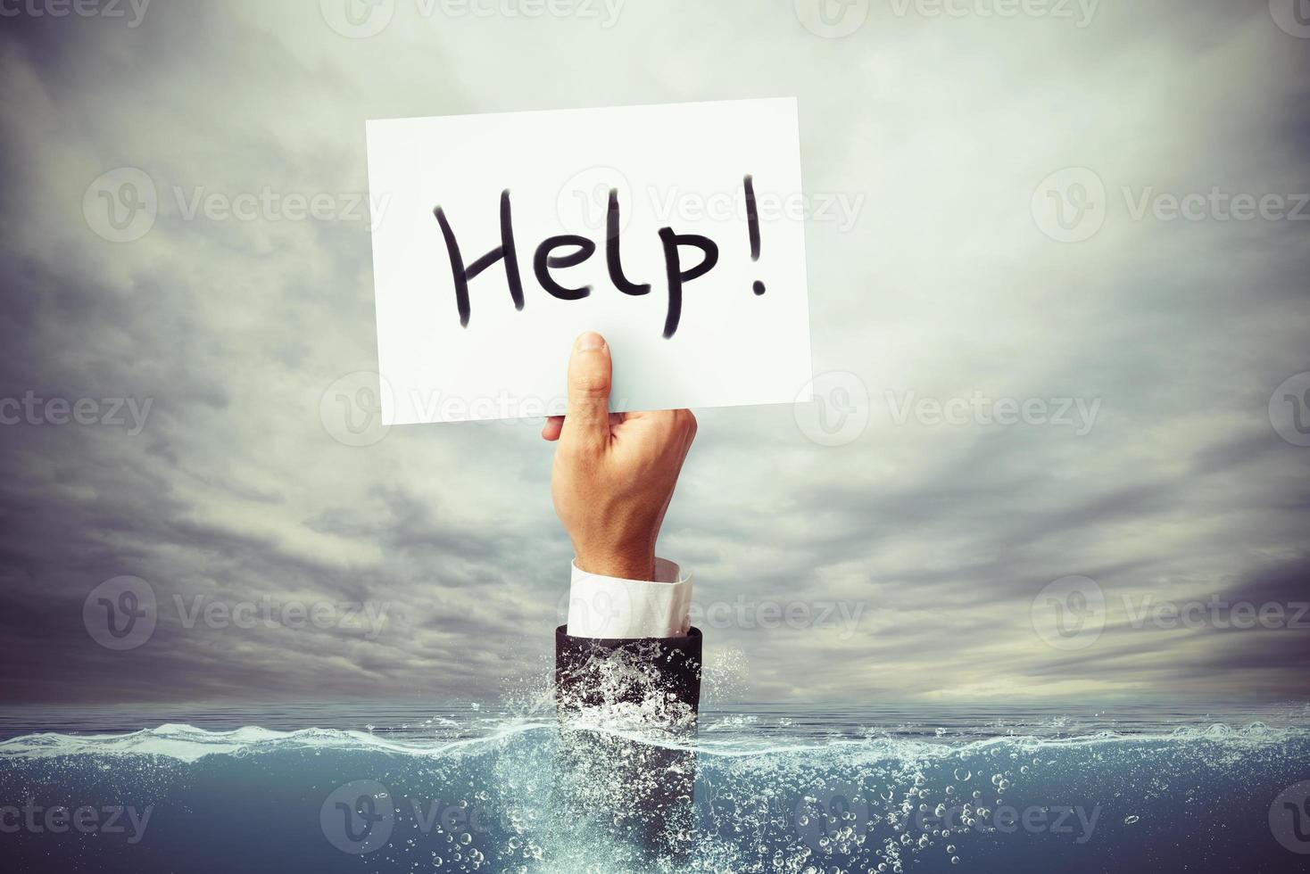 Businessman drowning in the sea with a hand holding a sheet of paper with help written photo
